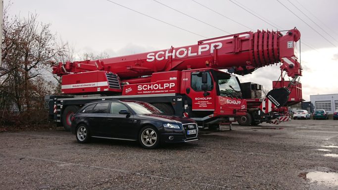 Roter Kran neben einem schwarzen Auto auf einem Parkplatz.